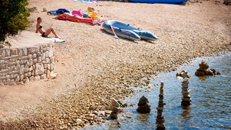 A person relaxing on a rocky beach with kayaks and stacked stones near the water