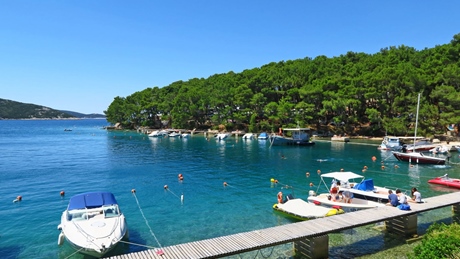 Boats docked along a wooden pier with lush greenery in the background on the island of Cres