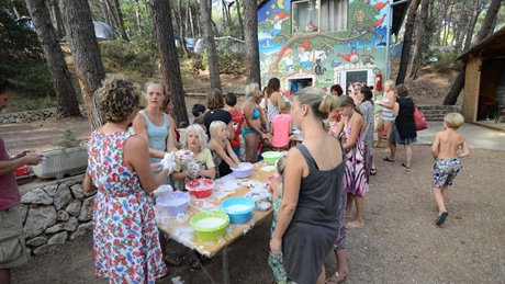 A group of people gather around a table with colorful bowls in a wooded area