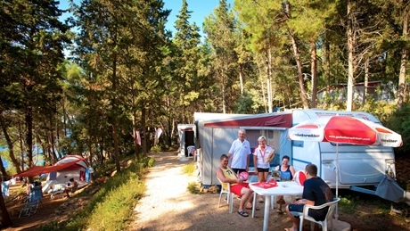 People enjoying a campsite near a forested area with caravans