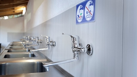 Multiple metal sinks with faucets and a warning sign on the wall