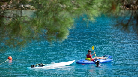 Person kayaking on clear blue water surrounded by trees