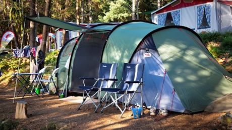 Camping setup with a green tent and chairs in a wooded area