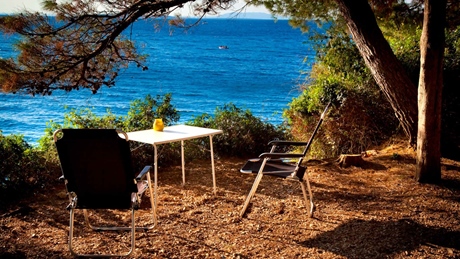Two chairs and a table overlooking the sea surrounded by trees