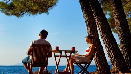 Couple sitting at a table by the sea under pine trees