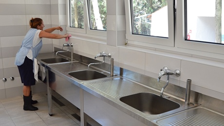 Person cleaning sinks in a tiled room