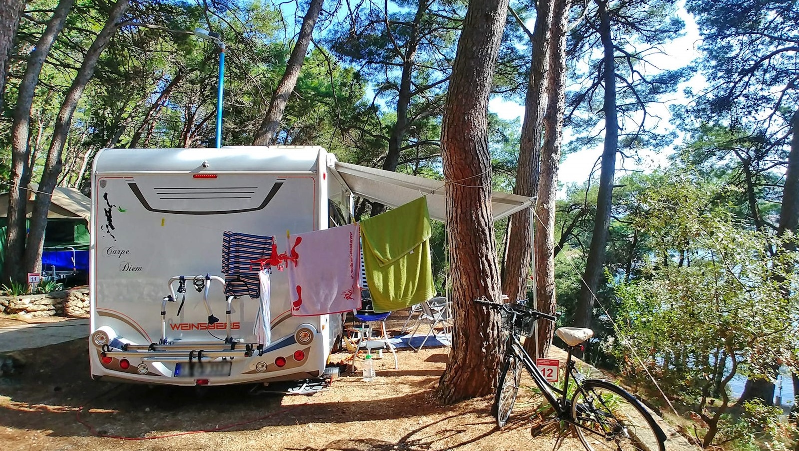 Wohnmobil auf einem bewaldeten Campingplatz mit aufgehängter Wäsche und einem Fahrrad in der Nähe