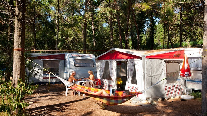 People relaxing outside a caravan in a forested campsite