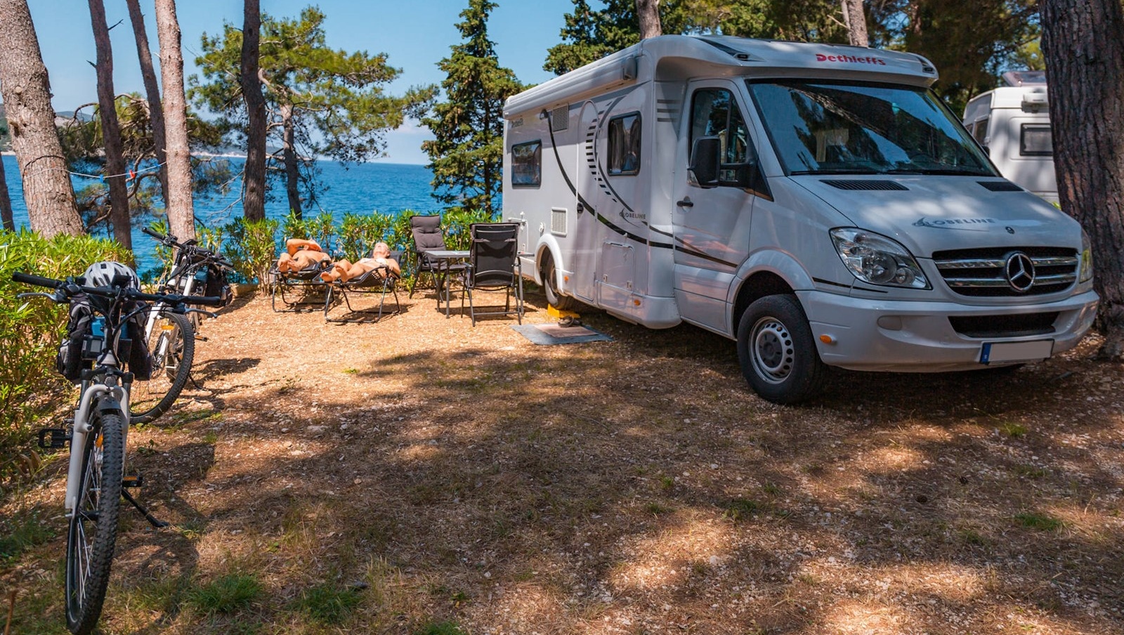 Camper van parked in a wooded area near the sea at Bijar with bicycles and outdoor seating