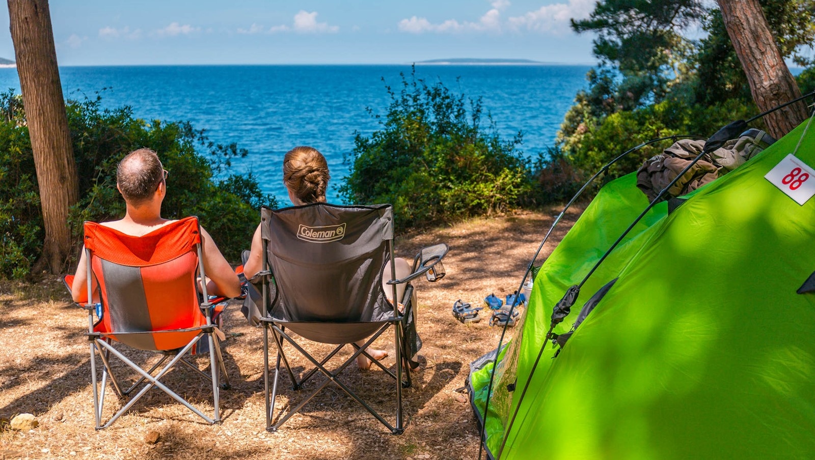 Two people sitting in camping chairs near a tent overlooking the sea at Bijar