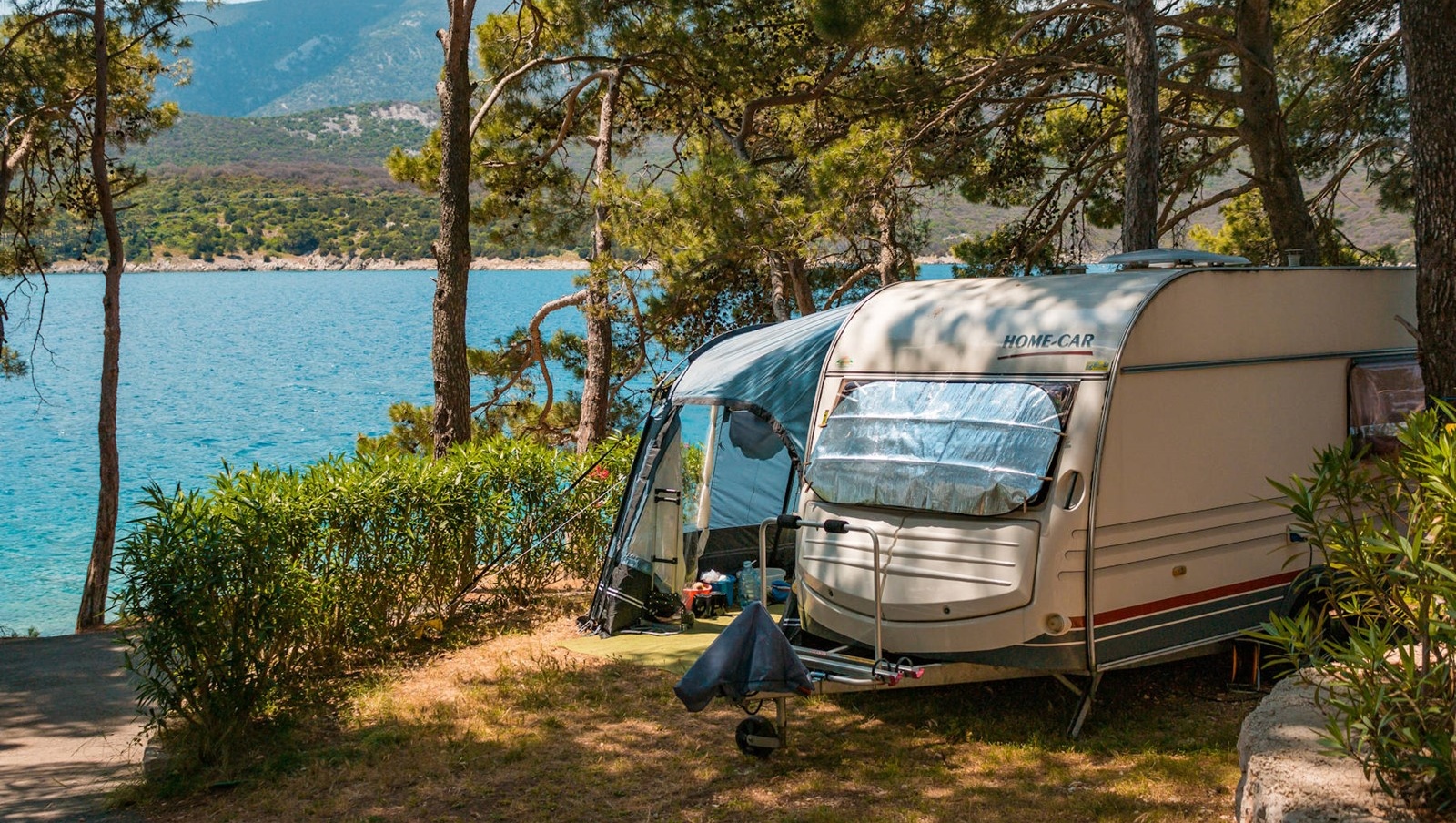 A camper trailer set up near the sea surrounded by trees