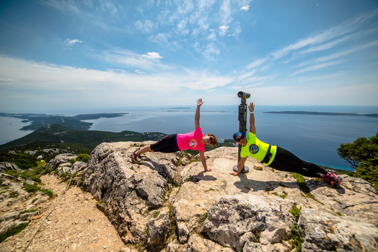 Two people doing side planks on a rocky hill with a view of the sea